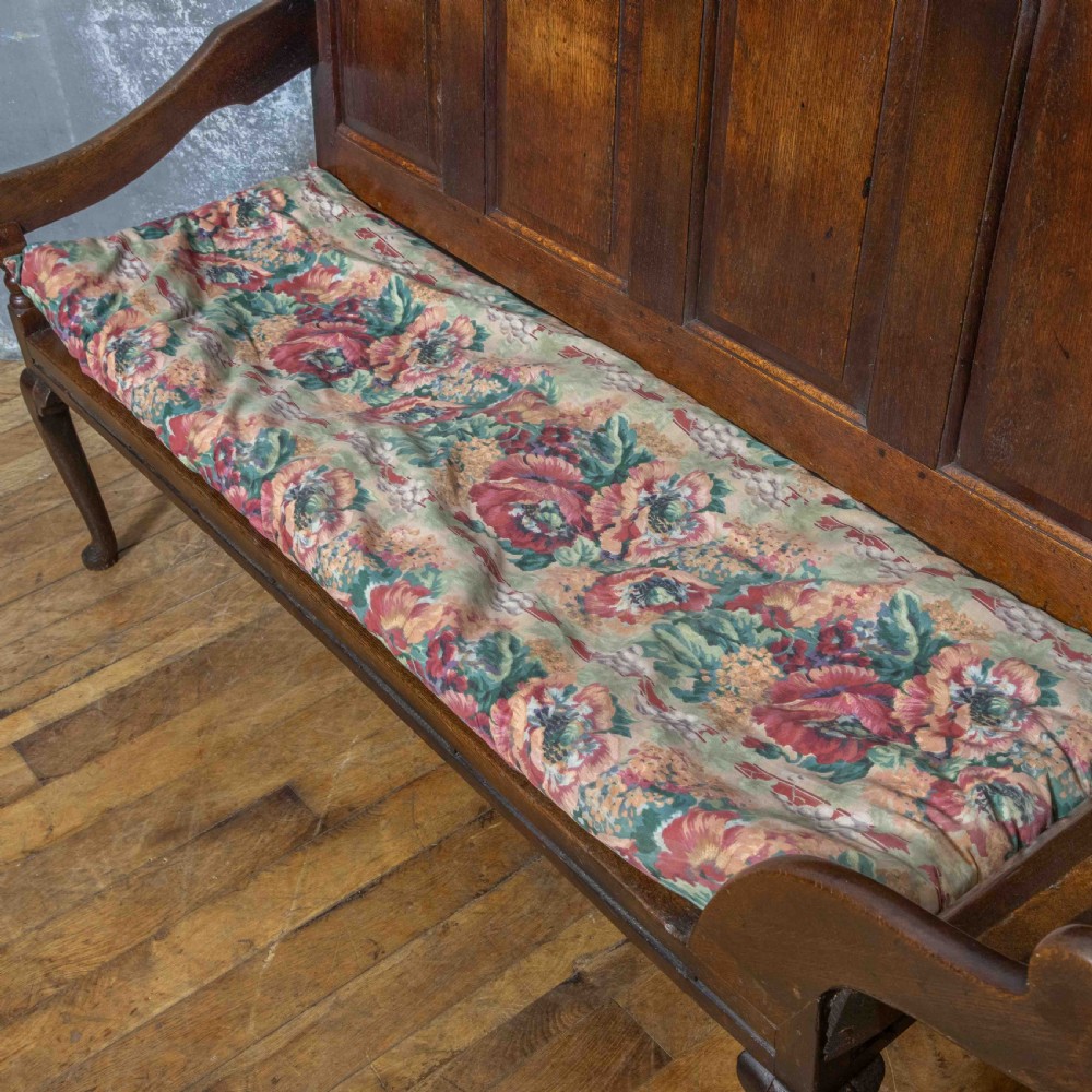 An antique dark oak sleeper settle featuring a high panelled backrest, cabriole front legs, and a floral upholstered cushion. View IX