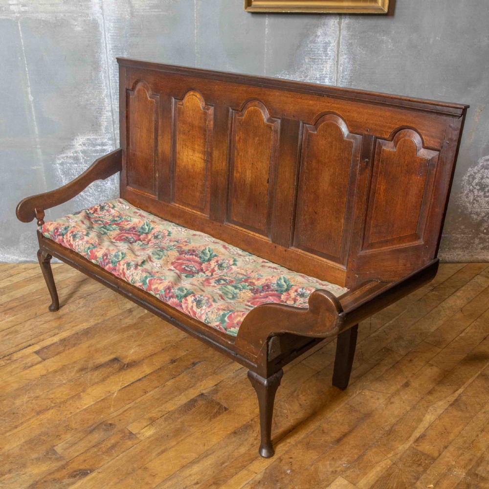 An antique dark oak sleeper settle featuring a high panelled backrest, cabriole front legs, and a floral upholstered cushion. View XI