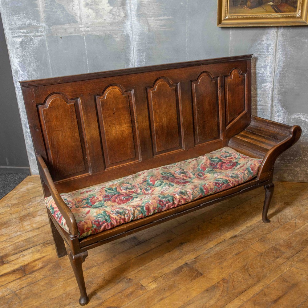 An antique dark oak sleeper settle featuring a high panelled backrest, cabriole front legs, and a floral upholstered cushion. View XII