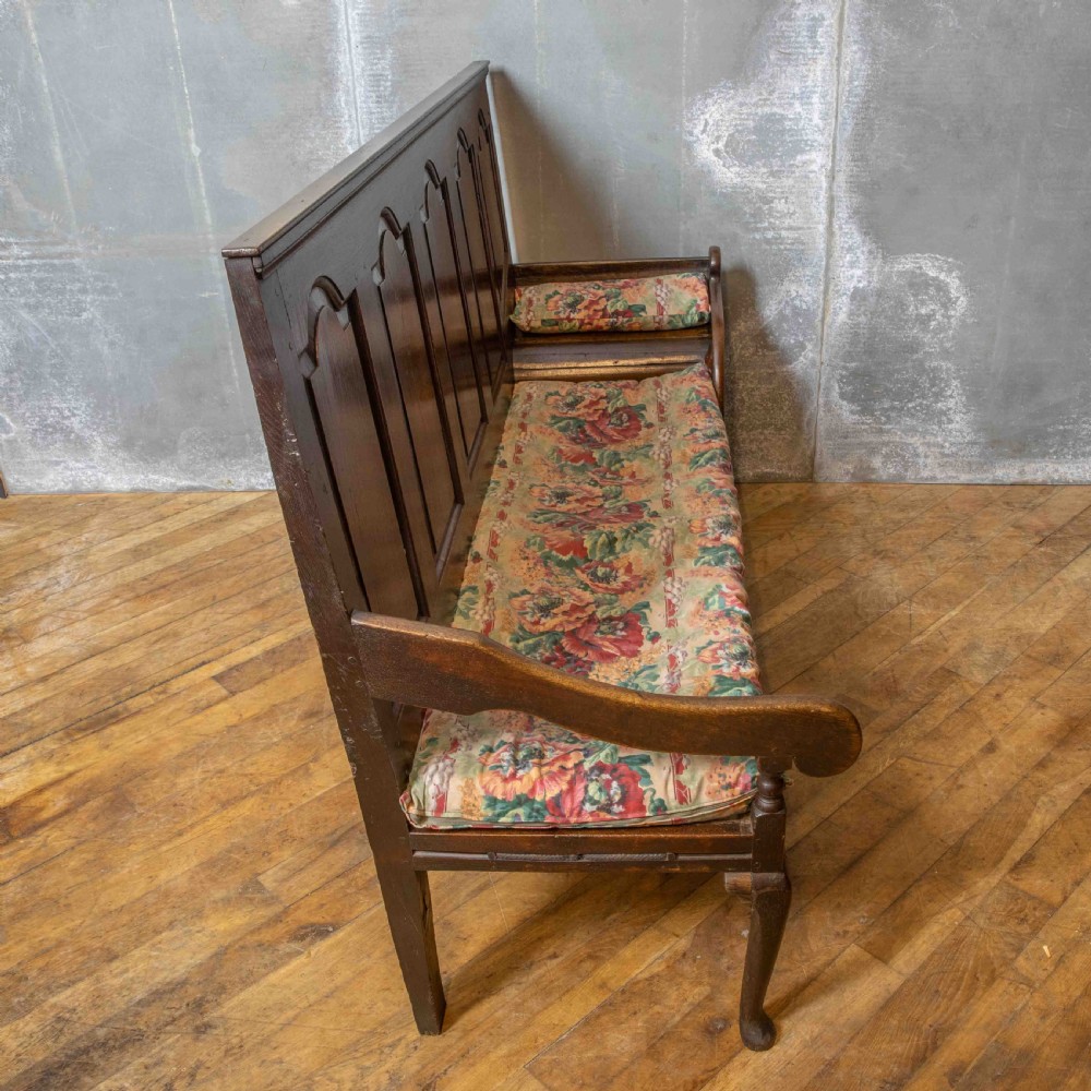 An antique dark oak sleeper settle featuring a high panelled backrest, cabriole front legs, and a floral upholstered cushion. View XIII