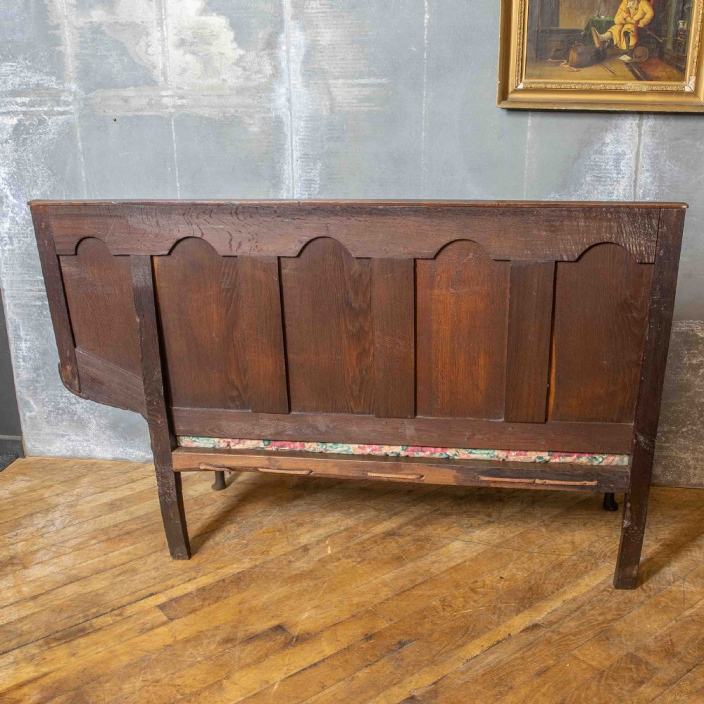 An antique dark oak sleeper settle featuring a high panelled backrest, cabriole front legs, and a floral upholstered cushion. View XIV