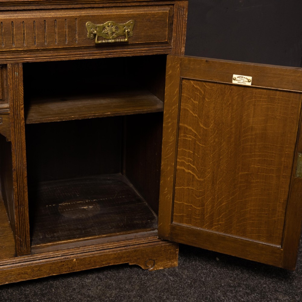An Edwardian carved oak sideboard featuring a mirrored back gallery, relief-carved door panels, multiple drawers with brass handles, and a central open display shelf. View III