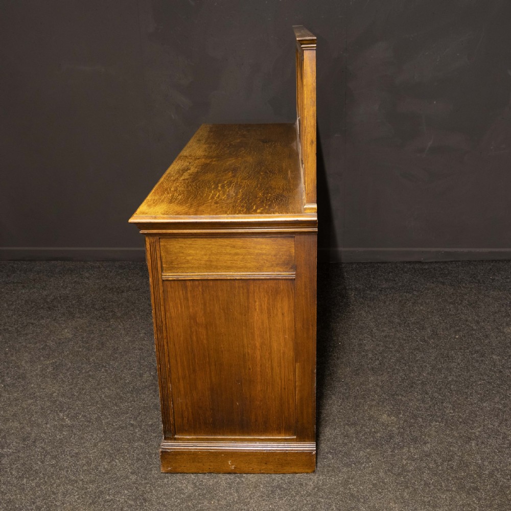 An Edwardian carved oak sideboard featuring a mirrored back gallery, relief-carved door panels, multiple drawers with brass handles, and a central open display shelf. View XI