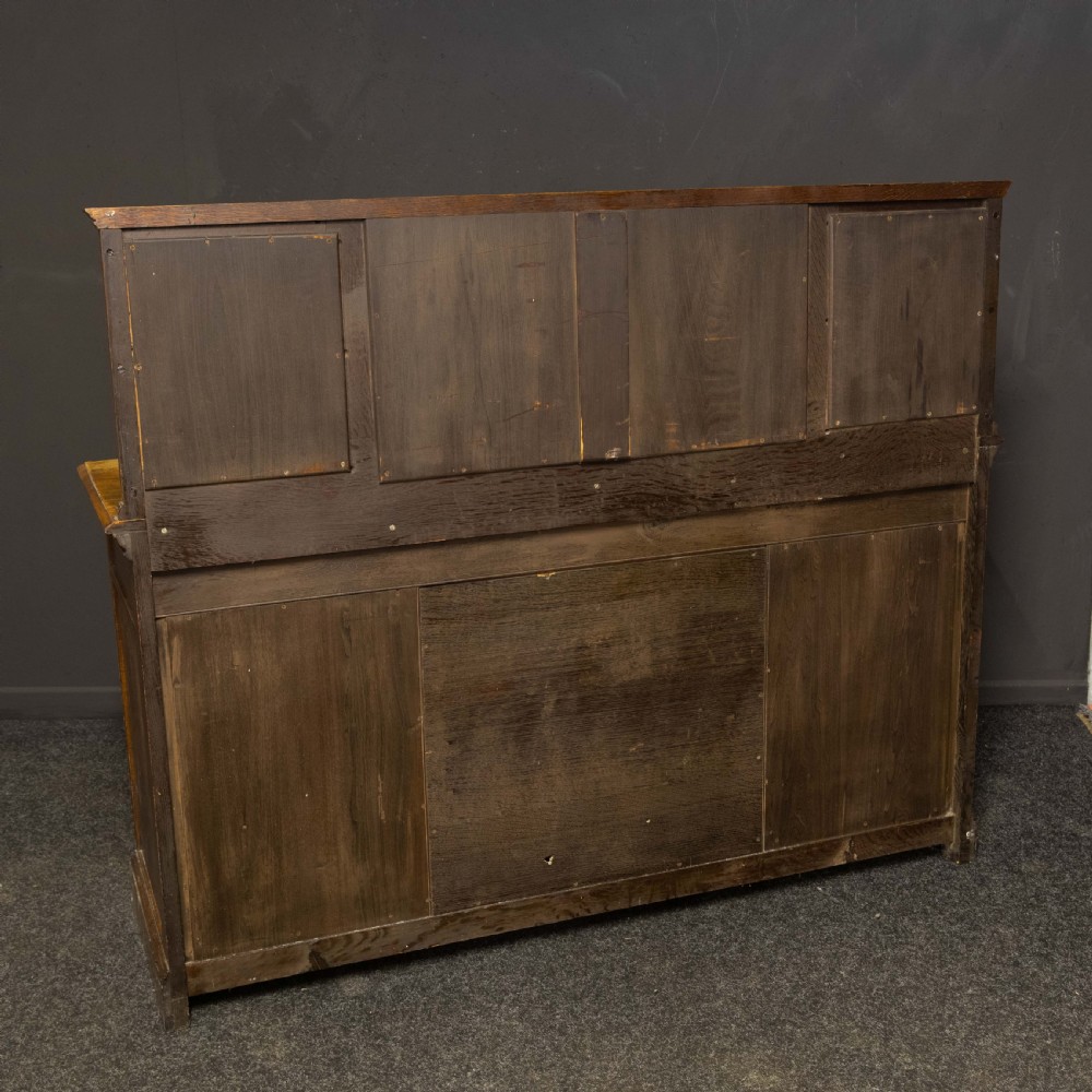 An Edwardian carved oak sideboard featuring a mirrored back gallery, relief-carved door panels, multiple drawers with brass handles, and a central open display shelf. View XII