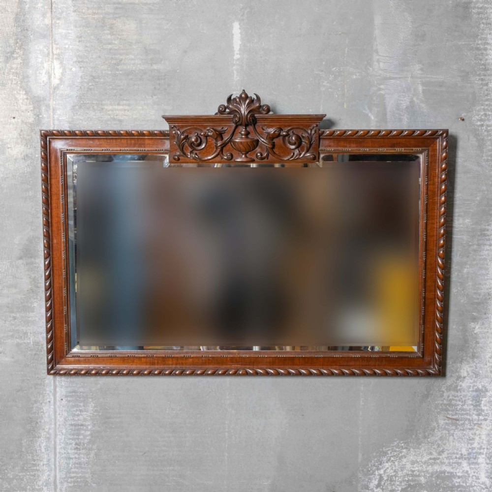 A rectangular Victorian Chippendale style mahogany wall mirror featuring a carved urn cresting, decorative scrollwork, and bevelled glass.