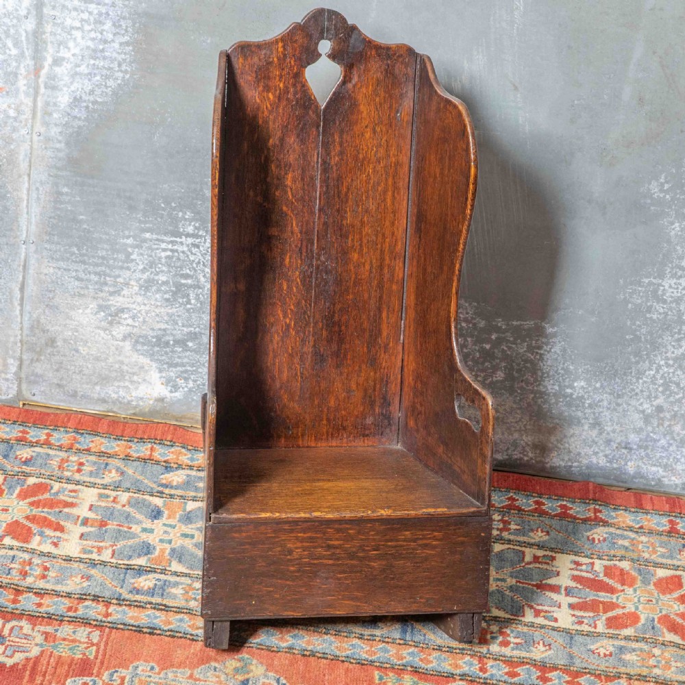 A small antique dark oak childs lambing chair featuring shaped wing sides, an enclosed back, cut-out carrying handles, and a solid box seat base. View II