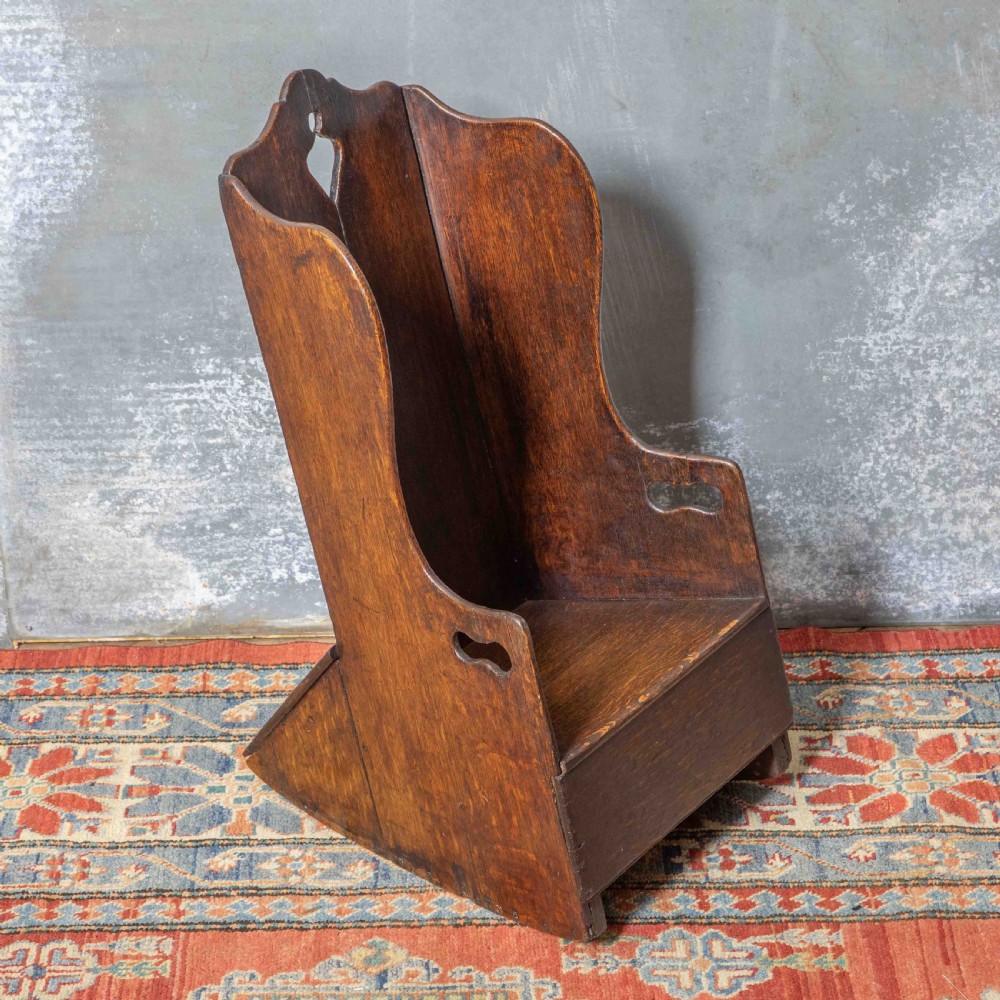 A small antique dark oak childs lambing chair featuring shaped wing sides, an enclosed back, cut-out carrying handles, and a solid box seat base. View III