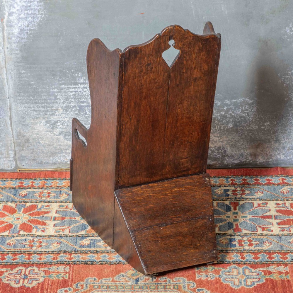 A small antique dark oak childs lambing chair featuring shaped wing sides, an enclosed back, cut-out carrying handles, and a solid box seat base. View V