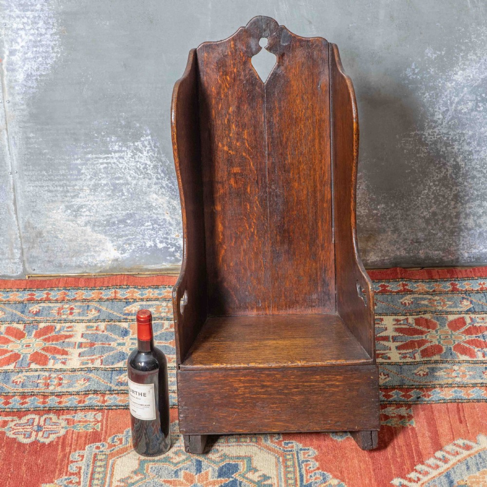 A small antique dark oak childs lambing chair featuring shaped wing sides, an enclosed back, cut-out carrying handles, and a solid box seat base. View VI
