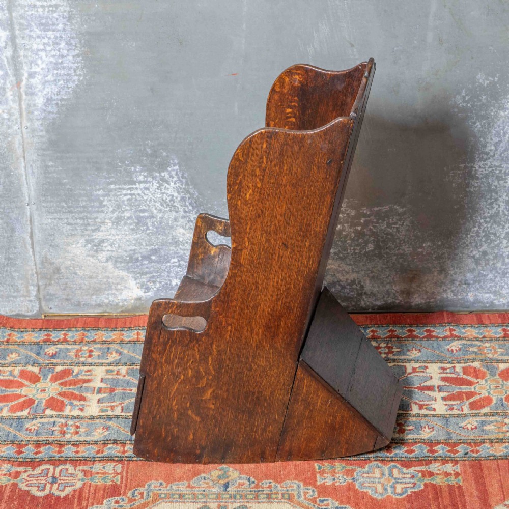 A small antique dark oak childs lambing chair featuring shaped wing sides, an enclosed back, cut-out carrying handles, and a solid box seat base. View VII