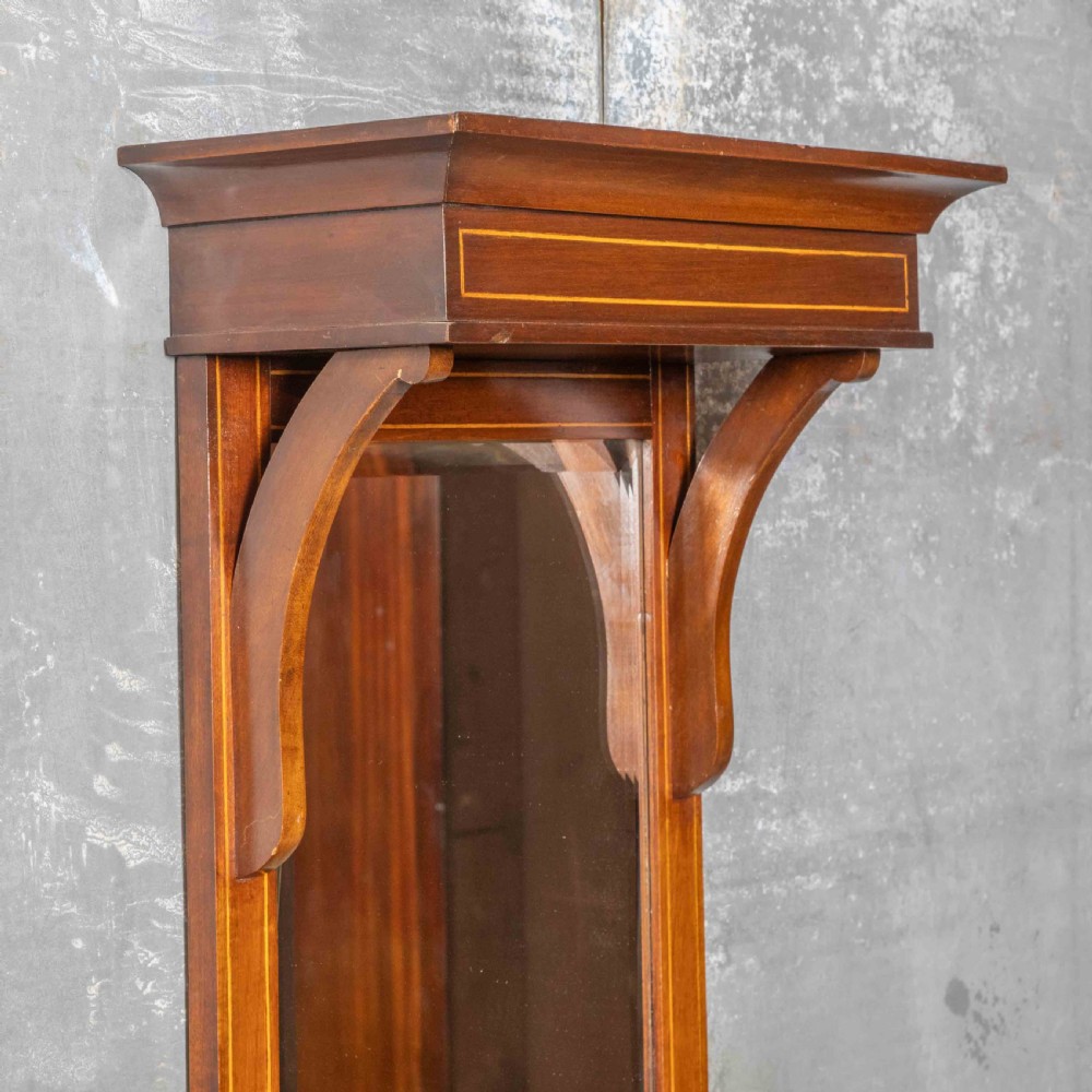 An Edwardian wall-mounted mahogany mirror featuring a top shelf cornice, a central bevelled glass panel, and a carved foliate wooden panel at the base. View V