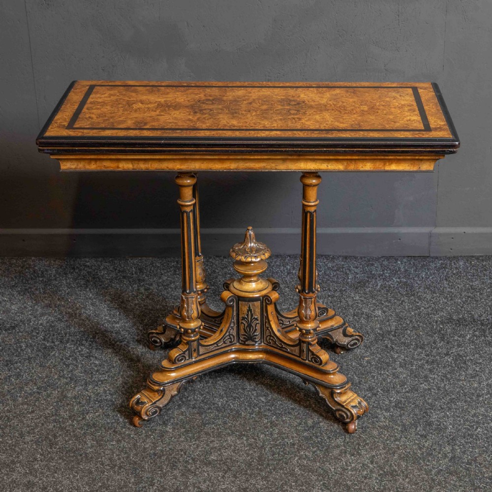 A Victorian Aesthetic Movement card table featuring burr walnut veneer, ebonised borders, turned support columns, and a central carved finial. View II
