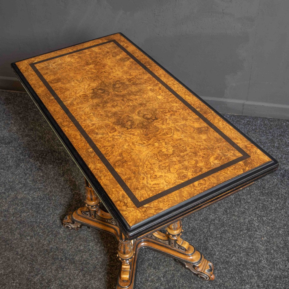 A Victorian Aesthetic Movement card table featuring burr walnut veneer, ebonised borders, turned support columns, and a central carved finial. View III