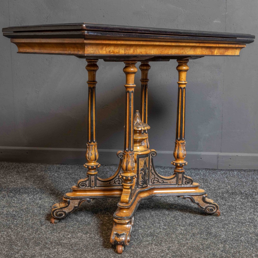 A Victorian Aesthetic Movement card table featuring burr walnut veneer, ebonised borders, turned support columns, and a central carved finial. View VIII