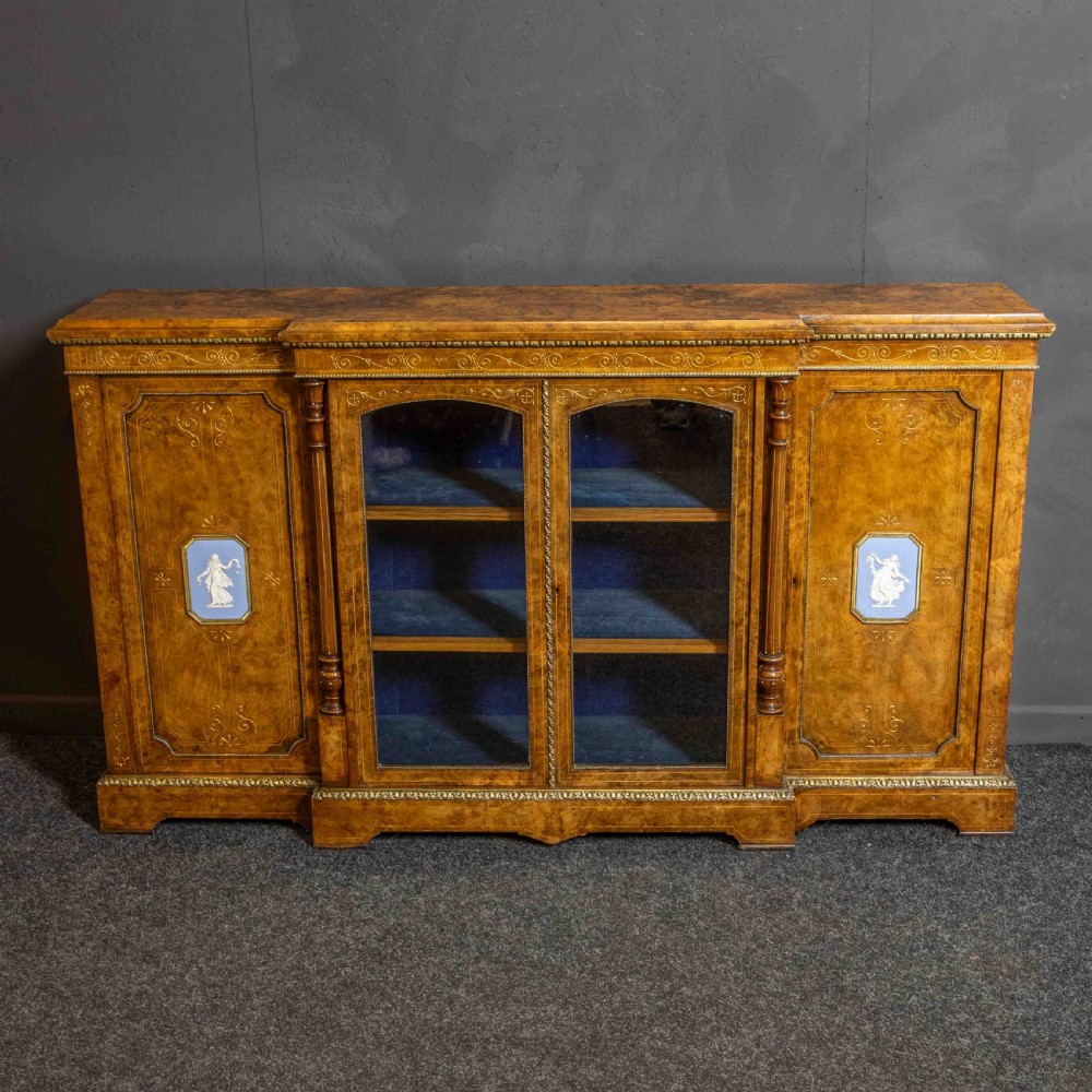 A Victorian burr walnut credenza featuring twin glazed central doors flanked by inlaid cupboard doors set with blue porcelain plaques.