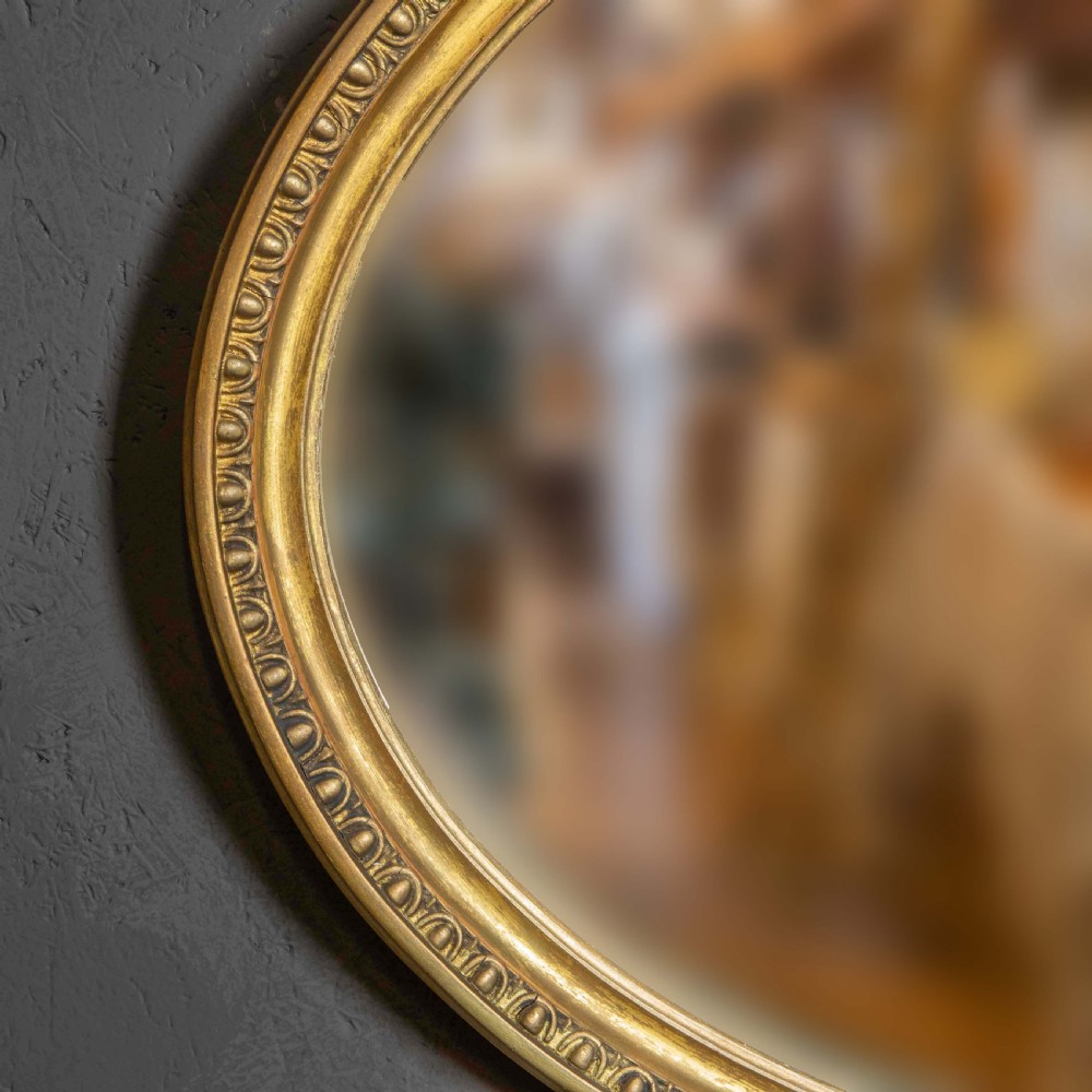 An oval gilded wall mirror decorated with an ornamental urn cresting at the top and floral swags along the lower edge. View III