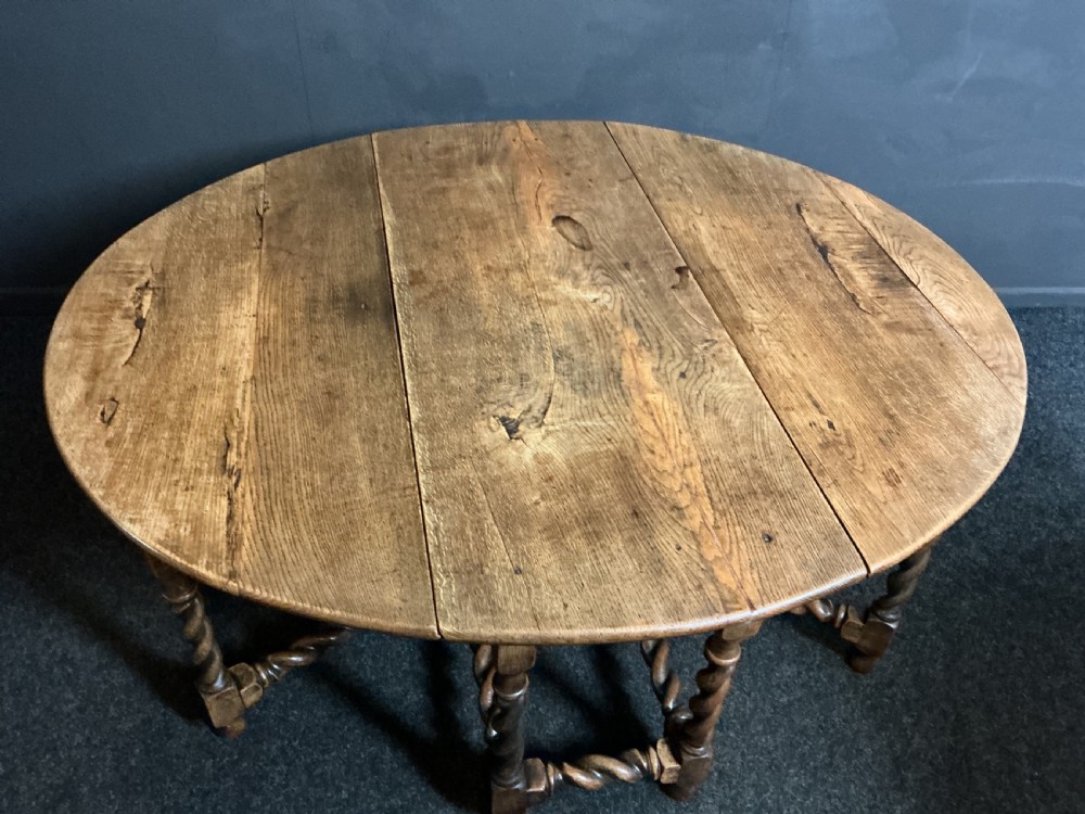 A large round antique oak gateleg dining table featuring drop-leaf flaps and decorative barley twist turned legs.
