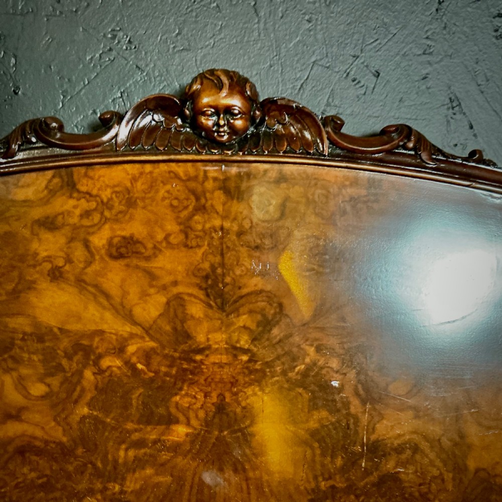 A king-size burr walnut headboard featuring an arched top rail with a central carved crest motif and prominent book-matched wood grain. View IV