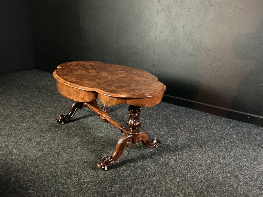 A low Victorian burr walnut coffee table featuring a serpentine top resting on turned carved supports and cabriole legs on castors.