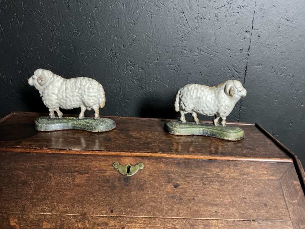 A pair of painted cast iron Victorian sheep ornaments standing on green bases.