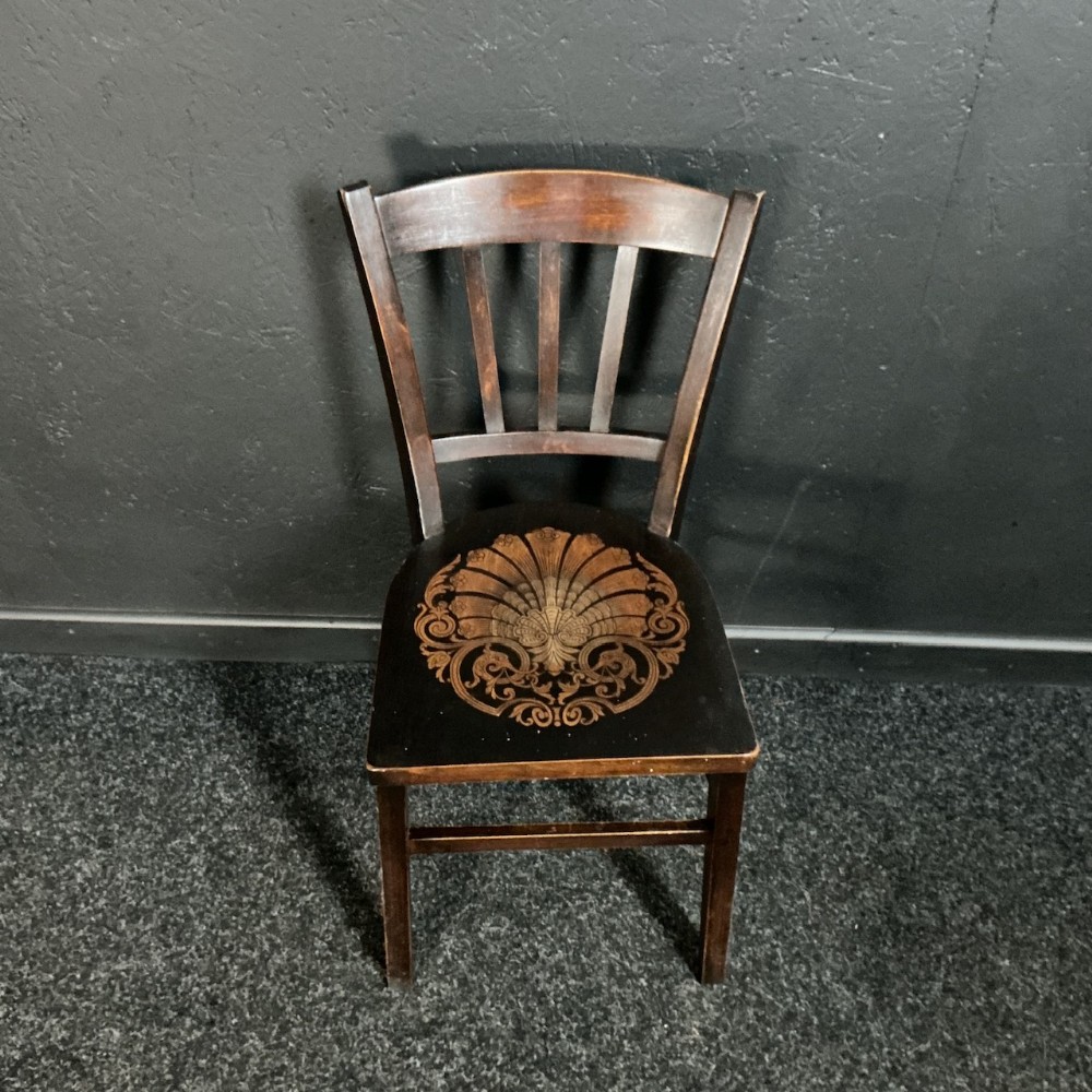 An Edwardian dark brown wooden bentwood side chair featuring a slat back and a decorative shell motif embossed on the seat panel.