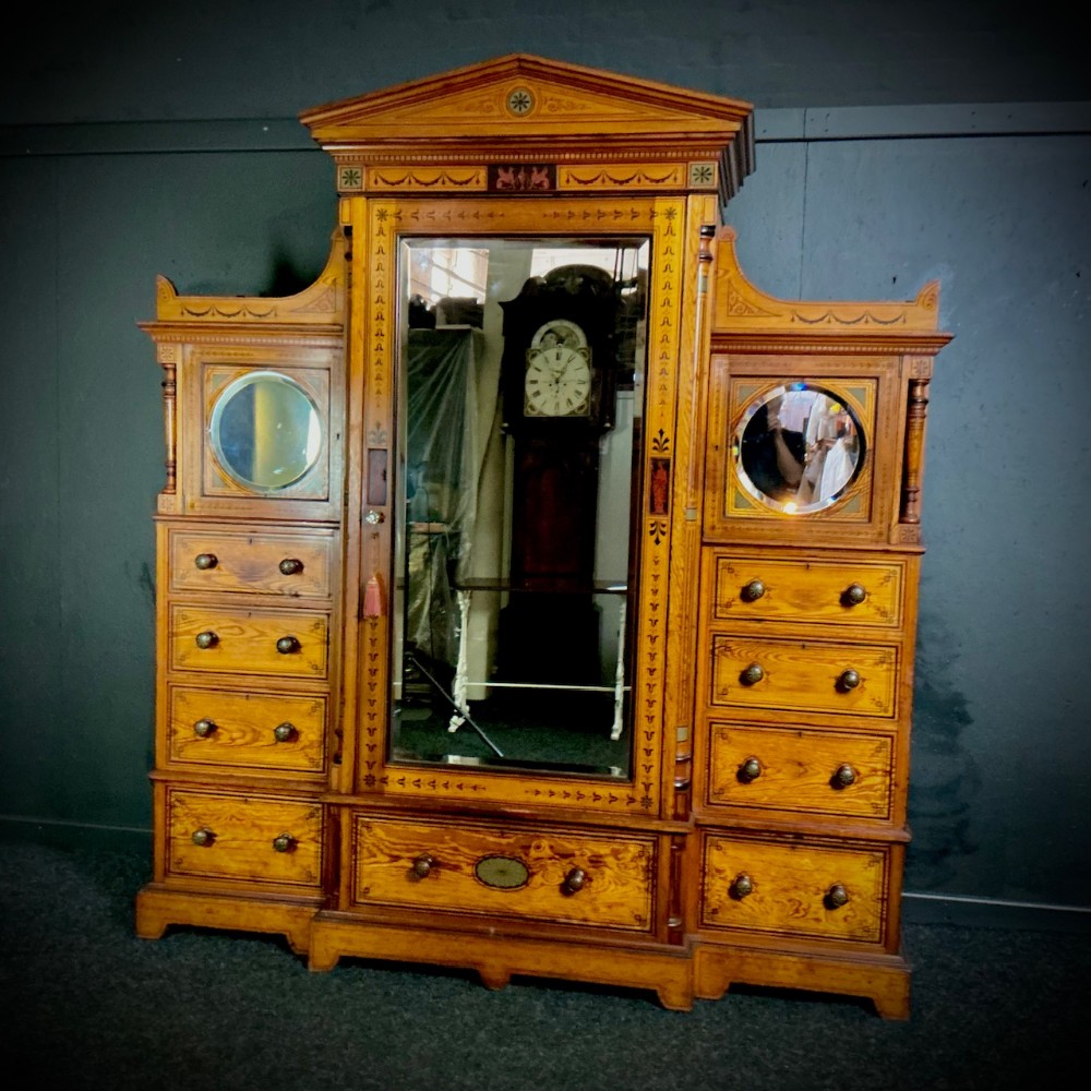 A Victorian pitch pine breakfront compactum wardrobe featuring a central mirrored door, pediment cresting, incised decorative inlay, and flanking drawers topped with circular inset mirrors.
