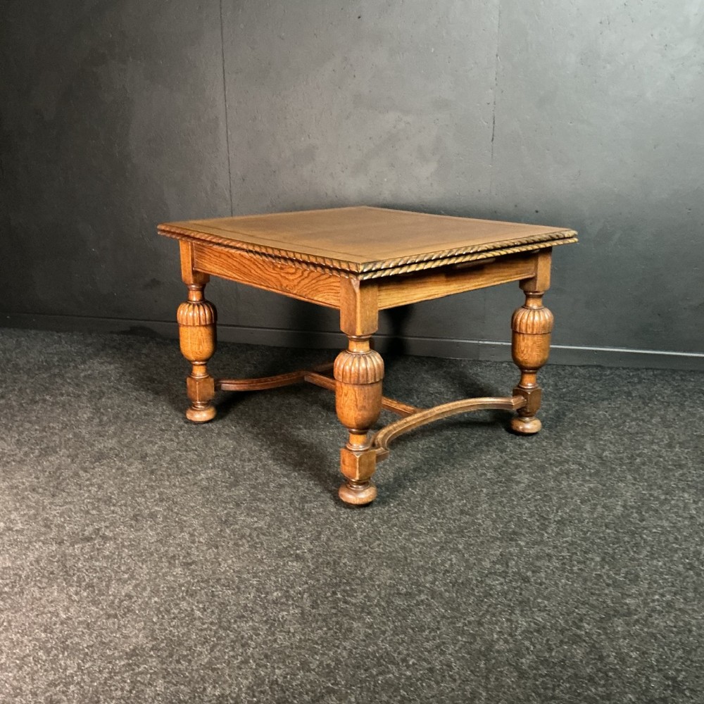 An antique medium brown oak draw-leaf dining table with carved rope-twist edge detailing, bulbous turned legs, and a low curved stretcher base.