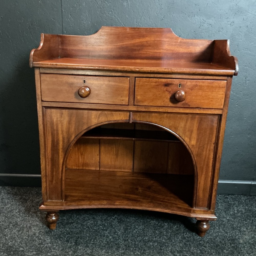 A Victorian mahogany dog kennel dresser featuring two top drawers with turned knobs above a open central arched recess and a low shaped splashback.