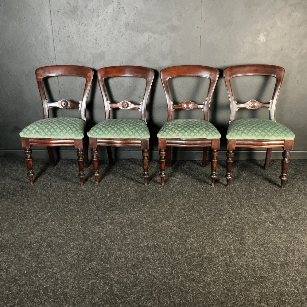 A set of four Victorian mahogany dining chairs featuring carved back rails, turned front legs, and green patterned fabric upholstered seats aligned in a row.