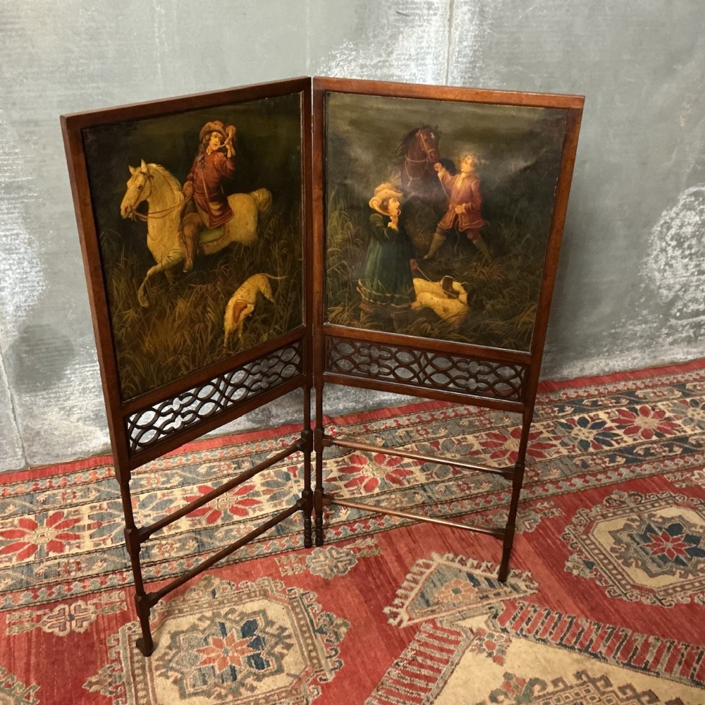 An Edwardian two-panel mahogany folding screen featuring inset oil paintings of equestrian figures and hounds above carved fretwork panels.