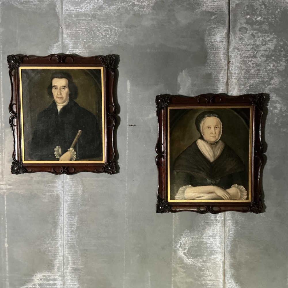 A pair of framed 18th-century oil portraits depicting a man holding an instrument and a woman wearing a shawl.