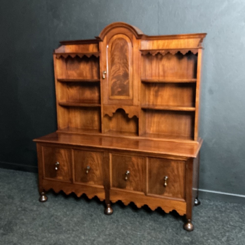 An Edwardian mahogany dresser featuring an upper shelf unit with a central arched cupboard door and a wide lower cabinet base on turned feet.