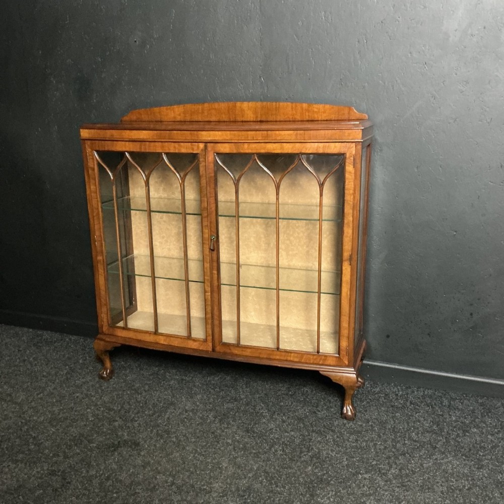 An early nineteenth-century walnut display cabinet featuring twin glazed doors with Gothic arched astragal glazing bars and cabriole legs ending in claw and ball feet.