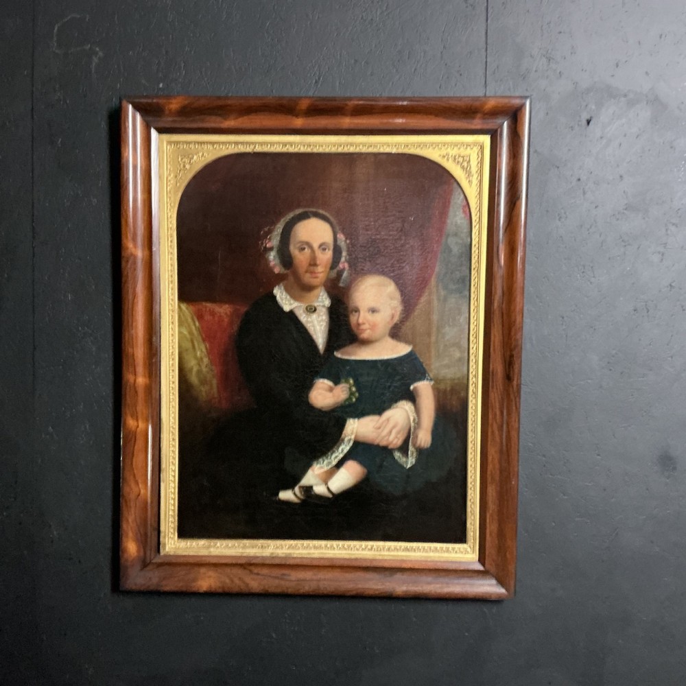 A 19th-century oil painting depicting a seated mother and child, encased in an arched gilt spandrel within a outer dark wood frame.