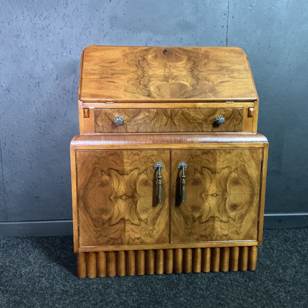 An Art Deco burr walnut slant-front writing bureau featuring a single drawer above a double-door cabinet and a reeded plinth base.