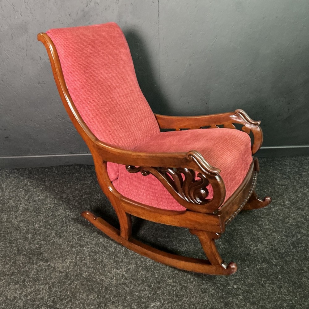 A Victorian mahogany rocking chair featuring carved scrollwork armrests and red textured upholstery.