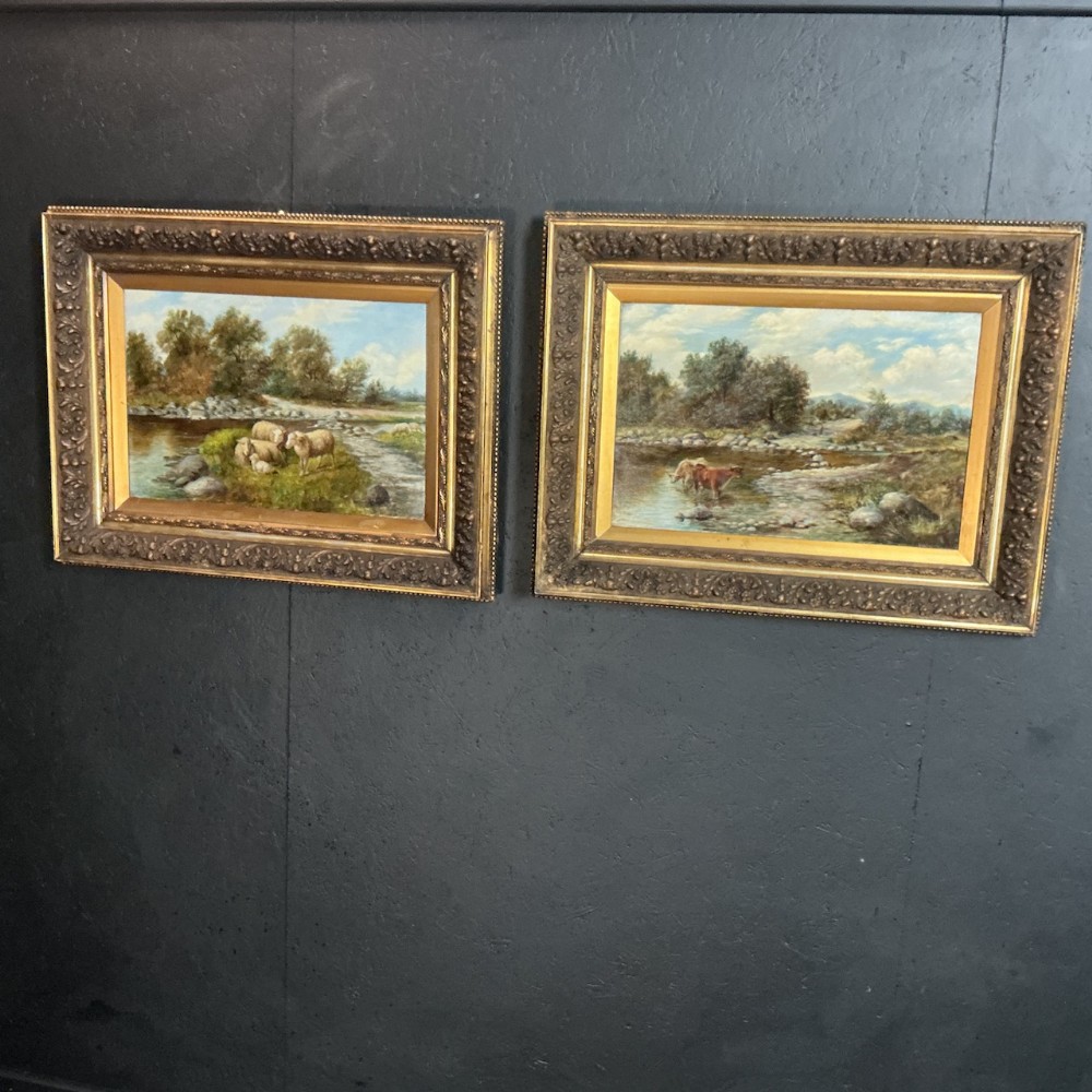 A pair of Victorian oil landscape paintings in ornate gilded frames depicting river scenes with cattle and sheep.