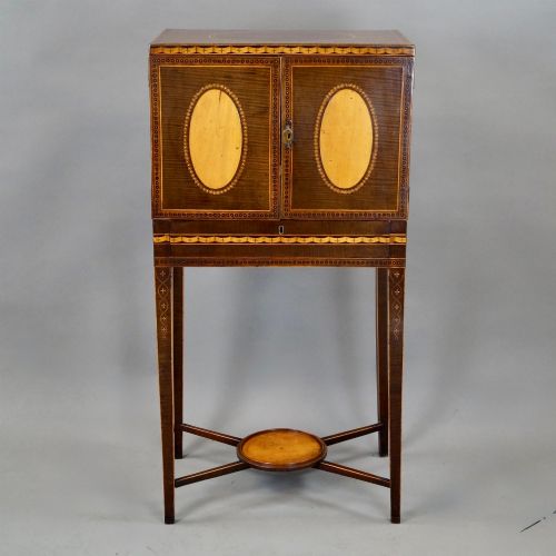 fig 1. A Sheraton period harewood cabinet on stand featuring twin cupboard doors with oval satinwood inlays and slender tapered legs connected by a circular stretcher tray.