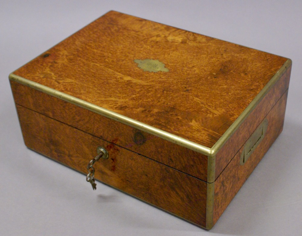 A rectangular 19th-century amboyna wood dressing box with brass bindings, a central brass cartouche, flush side handles, and an inserted steel key.