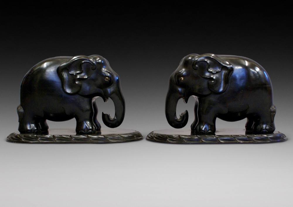 A pair of dark carved ebony elephant sculptures mounted on oval carved wood bases facing each other.