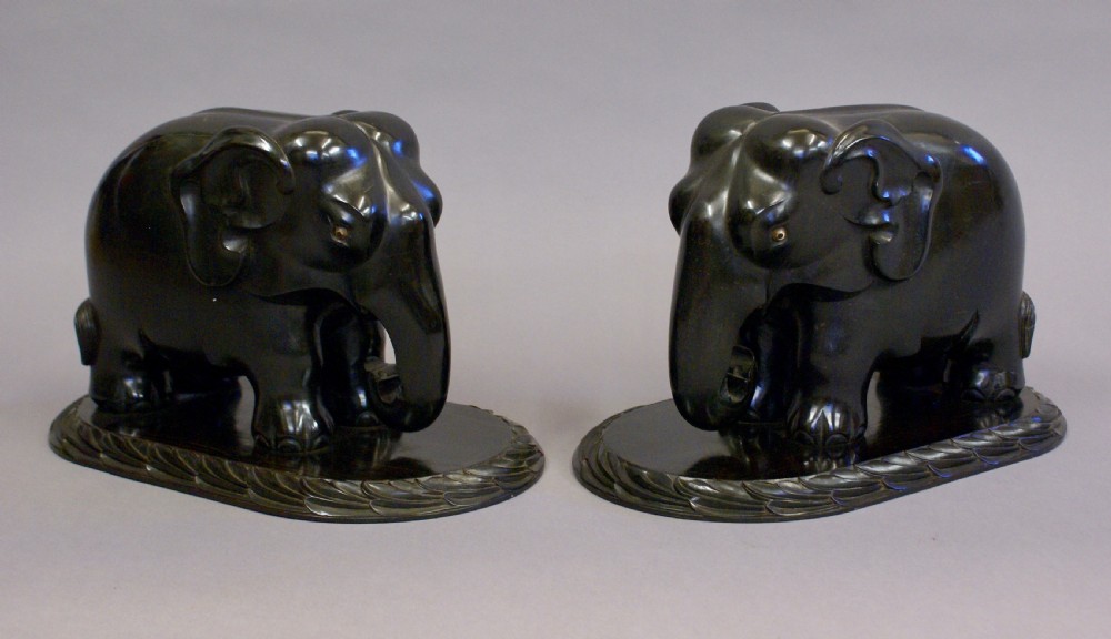 A pair of dark carved ebony elephant sculptures mounted on oval carved wood bases facing each other. View II