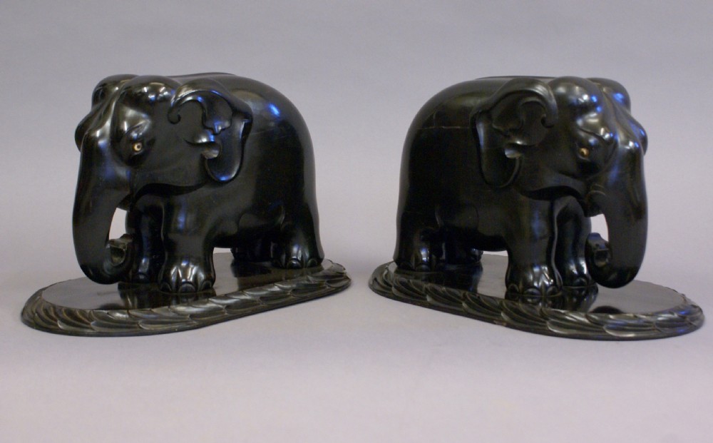 A pair of dark carved ebony elephant sculptures mounted on oval carved wood bases facing each other. View III