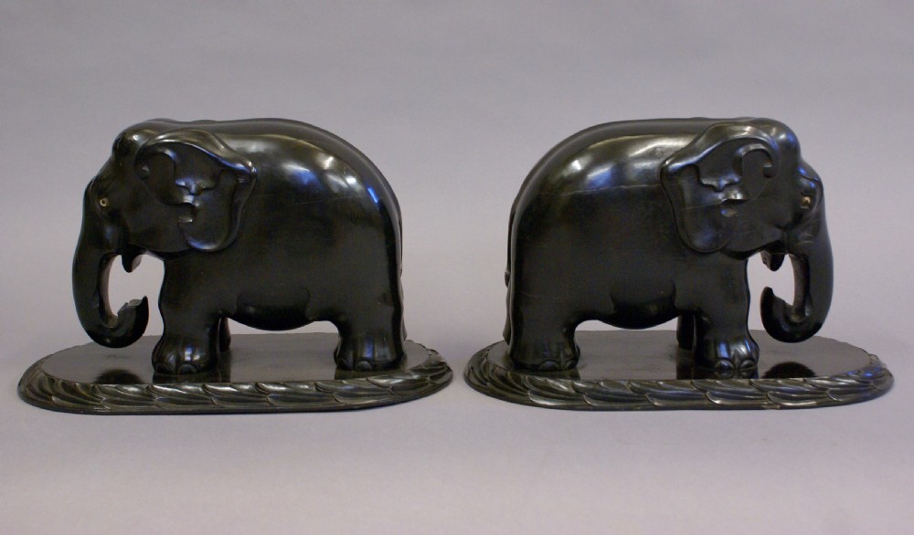A pair of dark carved ebony elephant sculptures mounted on oval carved wood bases facing each other. View V
