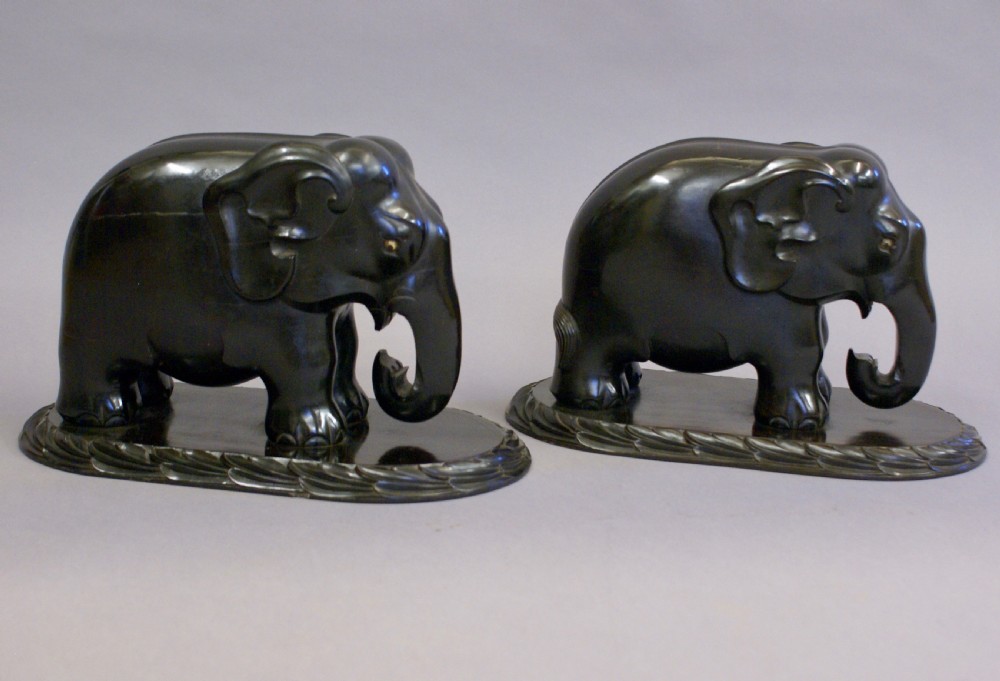 A pair of dark carved ebony elephant sculptures mounted on oval carved wood bases facing each other. View VI