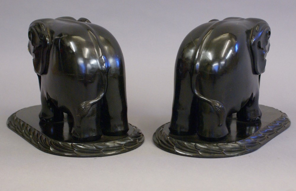A pair of dark carved ebony elephant sculptures mounted on oval carved wood bases facing each other. View VII