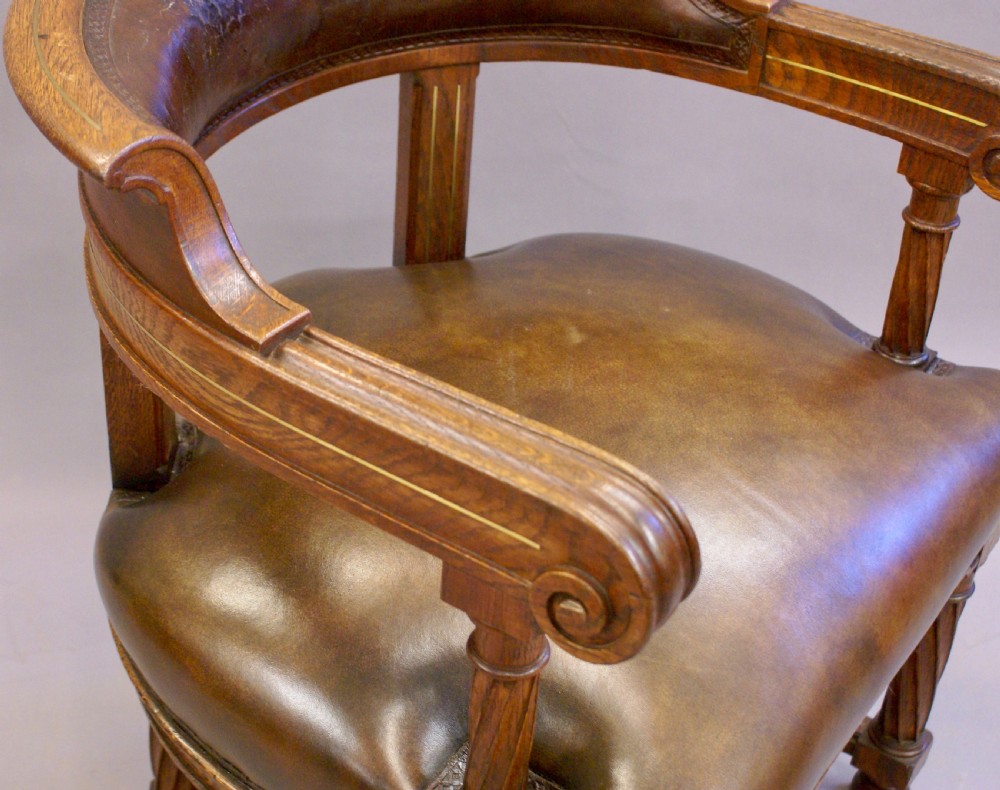 A 19th-century wooden armchair featuring a curved brown leather backrest, padded leather seat, scroll-ended arms, and brass stringing with clover motifs inlaid into the frame. View IV