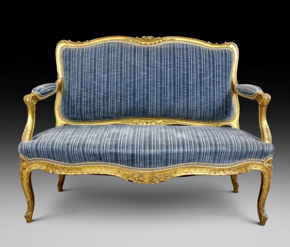 A 19th-century French Rococo-style giltwood sofa featuring a carved gold-leaf frame, cabriole legs, and blue striped fabric upholstery.