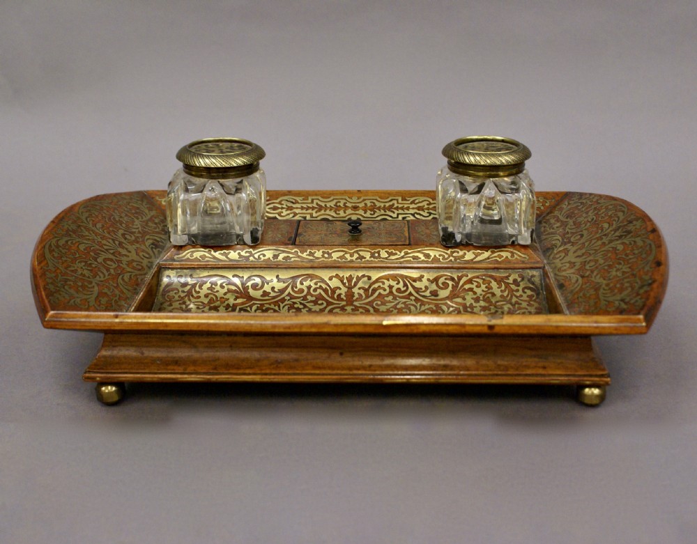 A Regency rosewood desk inkstand decorated with intricate floral brass inlay, featuring a curved pen tray, central lid, two clear cut-glass inkwells with brass caps, and brass ball feet. View III