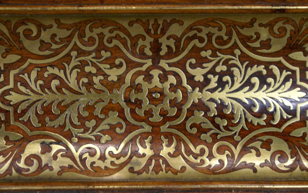 A Regency rosewood desk inkstand decorated with intricate floral brass inlay, featuring a curved pen tray, central lid, two clear cut-glass inkwells with brass caps, and brass ball feet. View VII