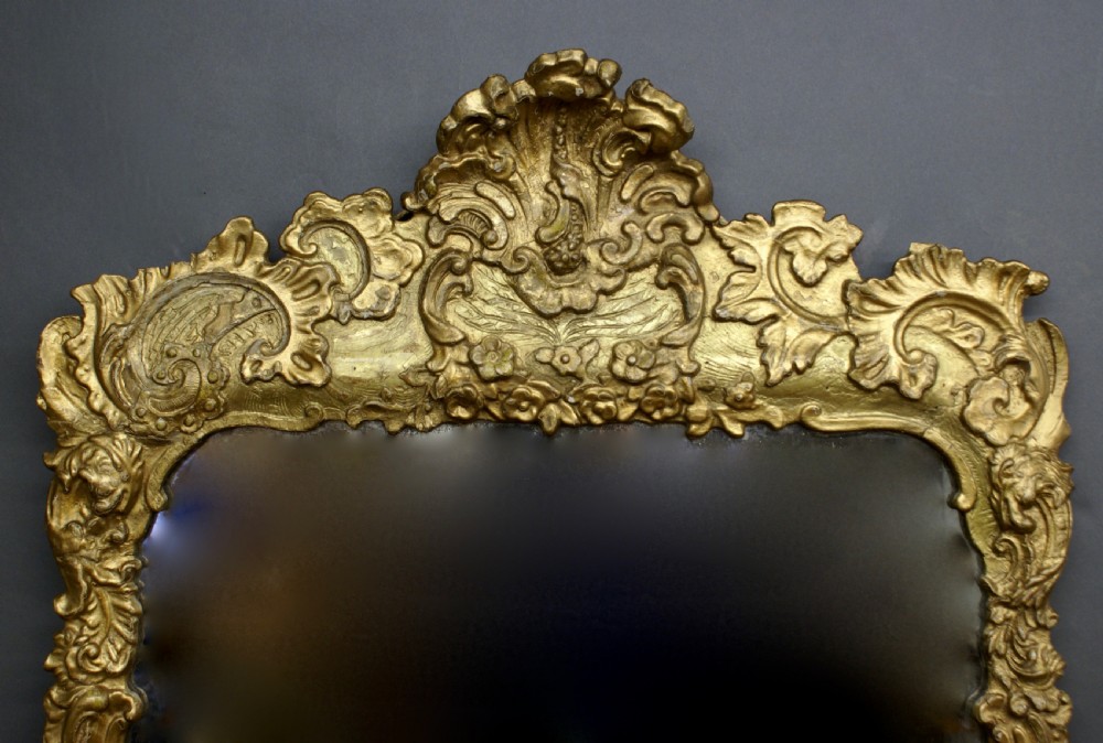 An 18th-century rectangular wall mirror featuring an intricate hand-carved giltwood frame adorned with rococo C-scrolls, foliage motifs, and a crest. View II